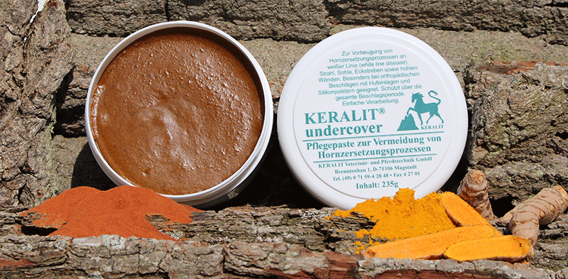 KERALIT undercover Pflegepaste KERALIT undercover Pflegepaste in einer runden Dose auf Baumrinde, umgeben von Kurkuma-Pulver.