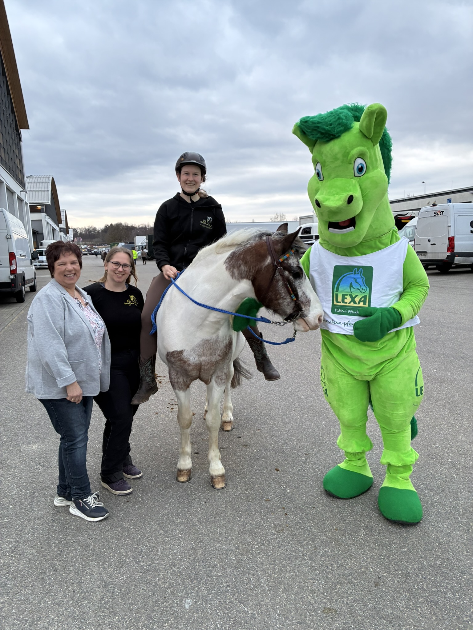 LEXA Maskottchen erkundet Messehalle mit verschiedenen Ständen im Hintergrund
